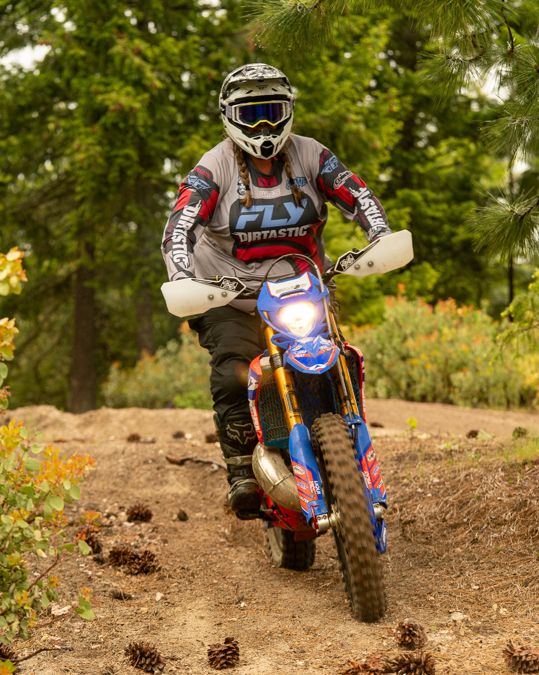 Person riding a dirt bike on a trail with trees and foliage in the background