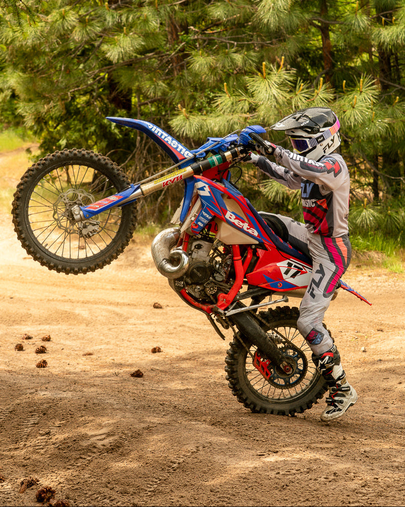 Person performing a wheelie on a dirt bike in a forested area