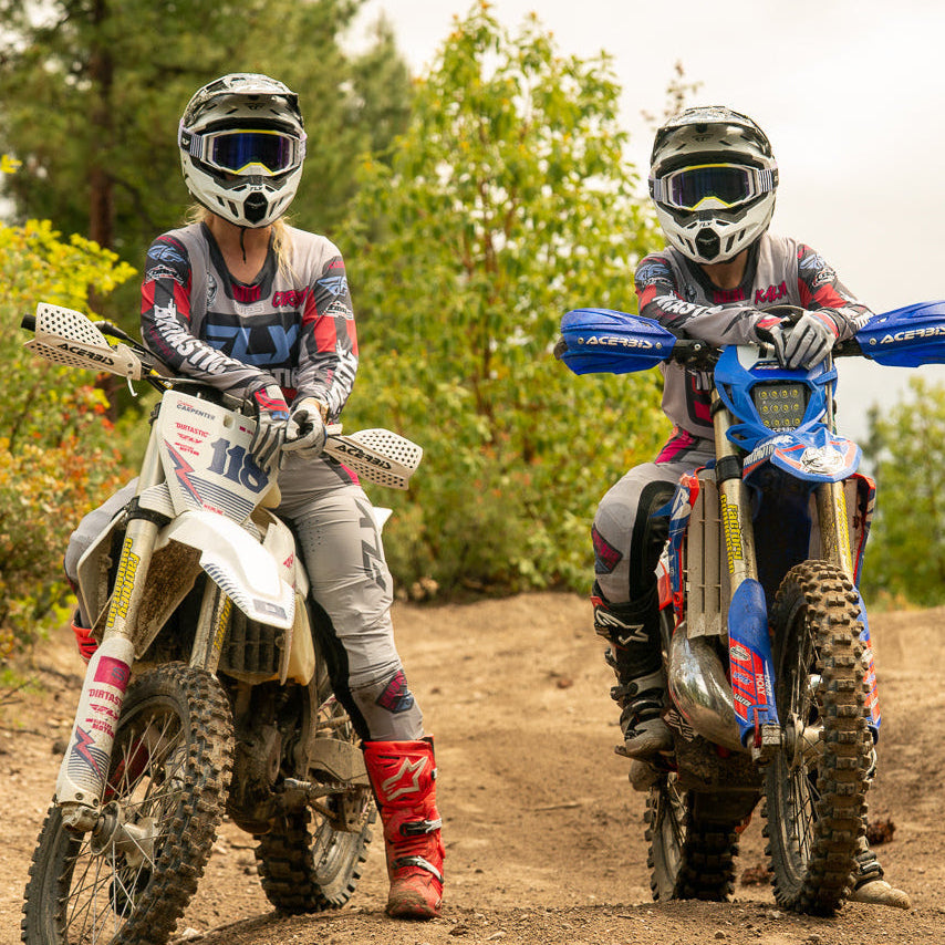 Two dirt bike riders on a trail with trees in the background